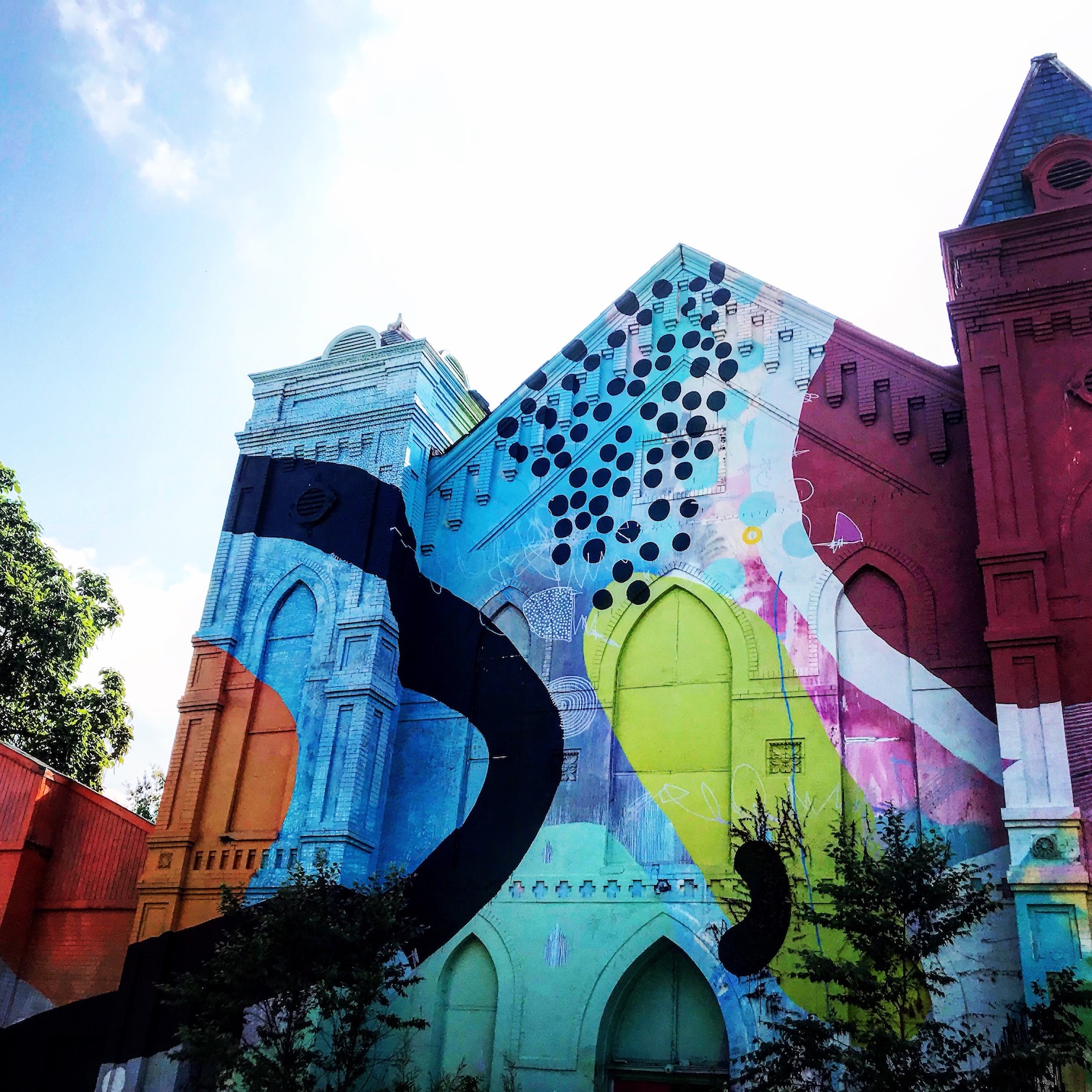 Exterior shot of an older building, may be a church, that is fully covered in a colorful abstract mural.